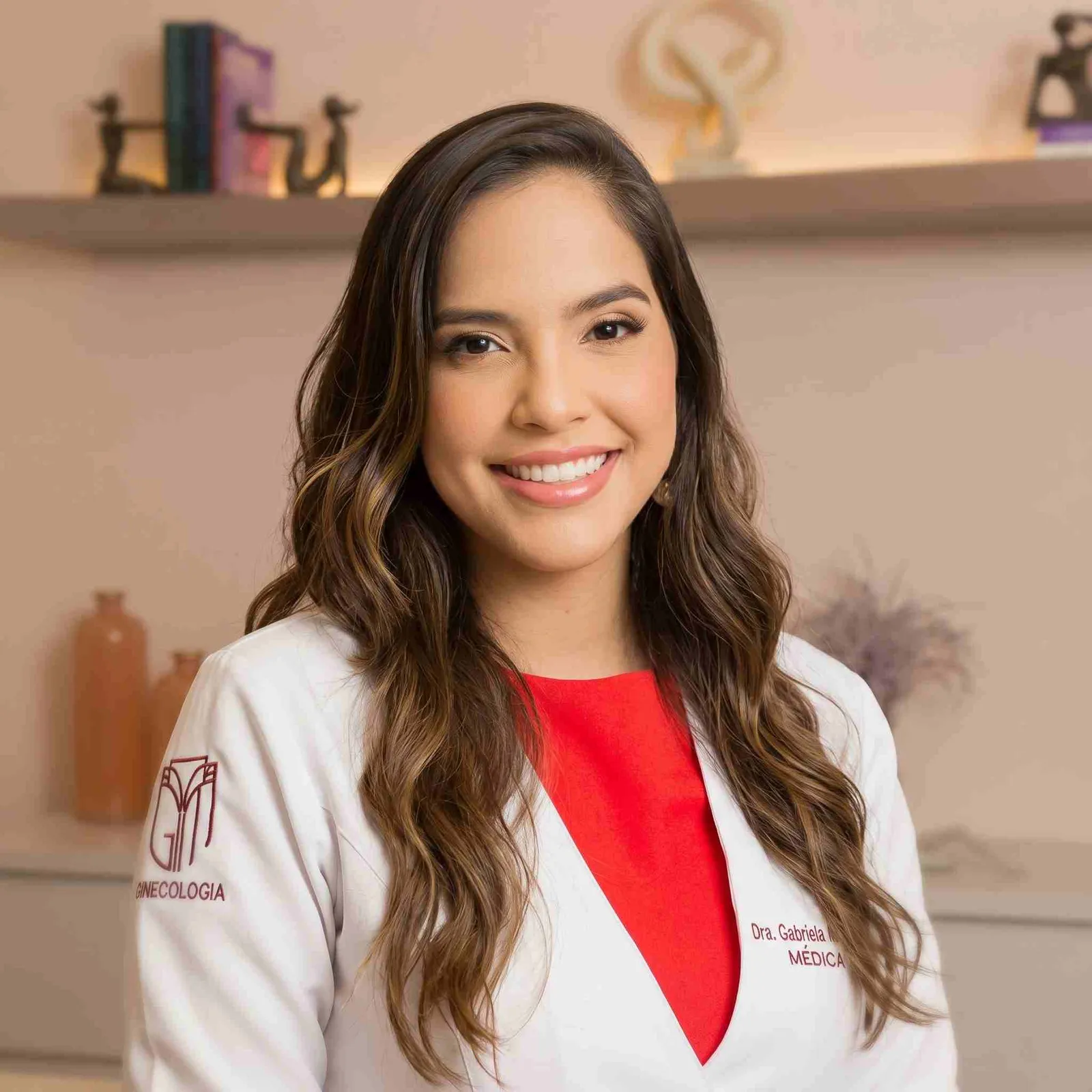 Retrato da Dra. Gabriela Gomes sorrindo, de jaleco branco, no consultório